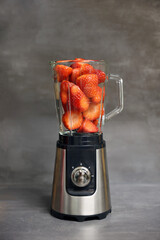 Stationary blender filled with slices of strawberries for making smoothie. Dark background, copy space