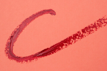 Brush strokes of red paint on peachy pink background, lipstick marks on paper