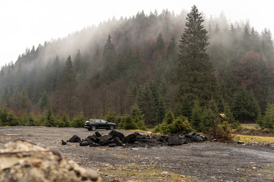Car standing in winter foggy forest.Mountains background