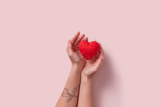 Red heart with thorns in tattooed woman's hands.