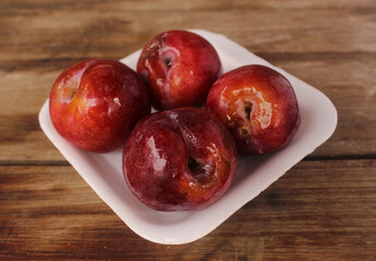 Red plum put in styrofoam plate on wooden floor