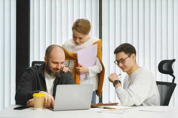 Diverse content coworkers browsing laptop at table
