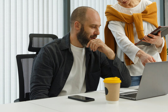 Male manager working on laptop and talking to colleague
