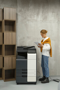 Young woman checking papers while printing in office
