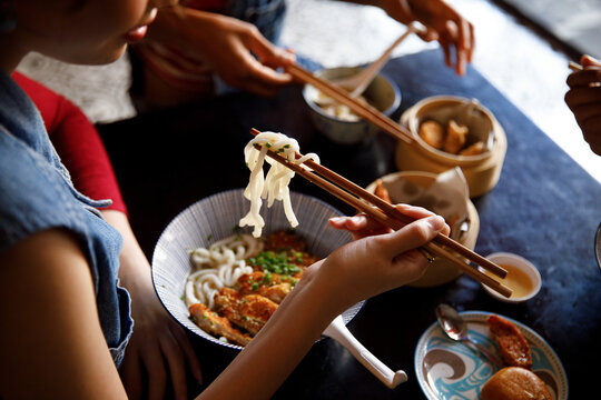 Hand of woman eating dim sum dumpling and thai ramen