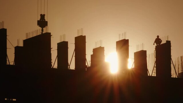 Silhouettes of builders working on construction site building at sunset, hard work. 