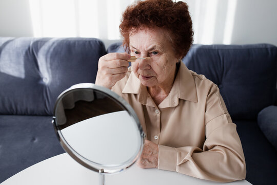 Senior Woman Applying Concealer Under EyesLooking In  The Mirror