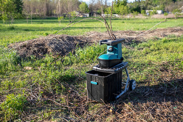 garden shredder was turned on in the net on the lawn next to a pile of dry branches that remained after pruning the garden during the spring work.