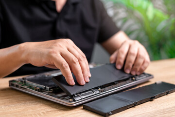 Laptop basic service of battery replacement, Technician Man holding the new battery and insert in the computer to repair laptop and remove the old part on the table to wait for removal, service work