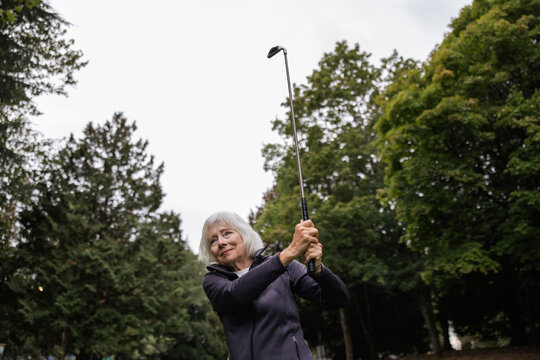 Silver haired woman playing golf on course.