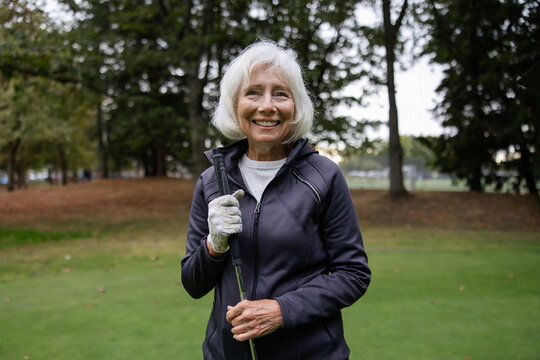 White haired woman smiling at the camera holding golf club.