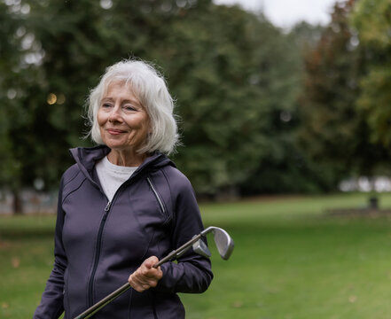 White haired woman smiling at the camera holding golf club.