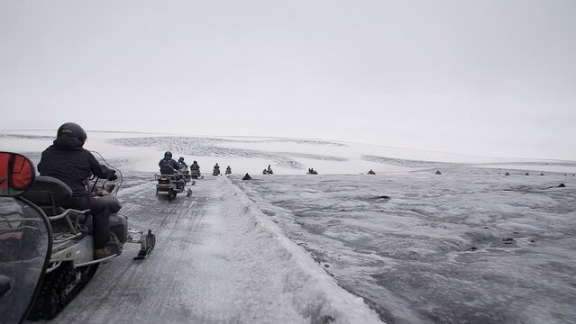 Group of tourists riding snowmobiles with a guide at Vatnajokull glacier in Iceland. Active sport, recreation, lifestyle.