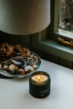 A scented candle burning in front of a widow indoors. 