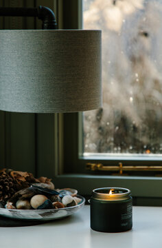 A scented candle burning in front of a widow indoors. 