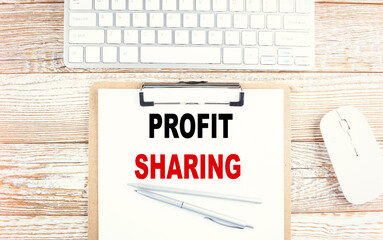 PROFIT SHARING text on a clipboard with keyboard on wooden background