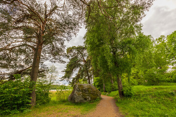 Beautiful view of summer landscape with lake view and large stone in forest on side of hiking trail. Sweden.