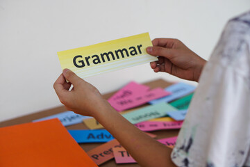 Closeup student's hands  hold English Grammar word card. Concept, education, learning, studying language. Education. Reading and memorizing strategy of learning process for kid. Practice makes perfect