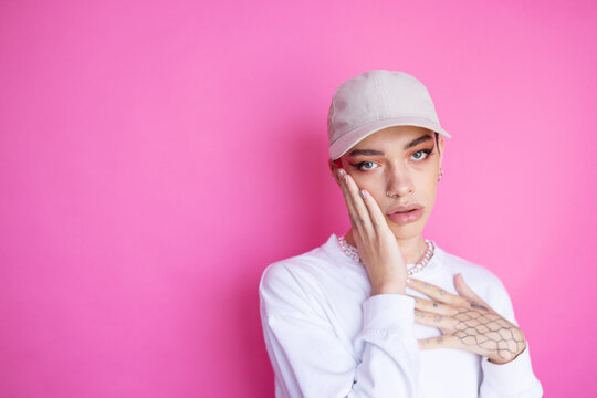 Extravagant non-binary man with makeup in cap on pink background