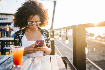 Hispanic woman using smartphone on restaurant terrace