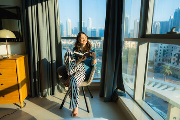 Woman sitting on chair and reading book at home 