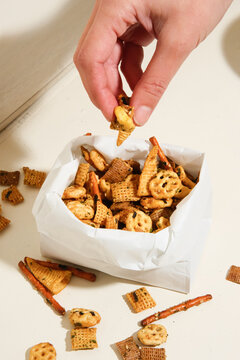 Hand grabbing Chex mix snack from paper bag. 