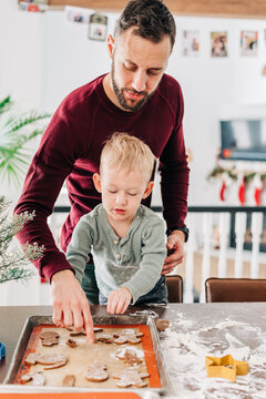 A father and son carefully lay cookie dough onto baking sheet