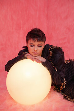 Androgynous brunette leaning on glowing sphere
