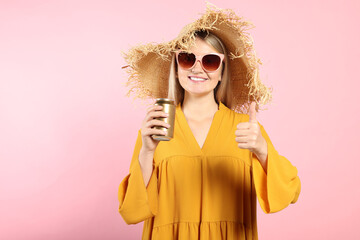 Beautiful happy woman holding beverage can and showing thumbs up on pink background