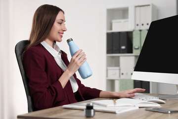 Woman holding light blue thermos bottle at workplace - obrazy, fototapety, plakaty