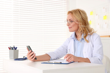 Doctor with glasses and smartphone consulting patient in clinic. Online medicine concept