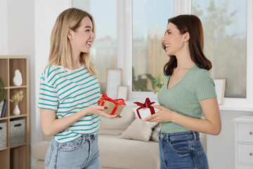 Smiling young women presenting gifts to each other at home