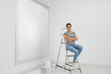 Woman sitting on metallic folding ladder indoors, space for text