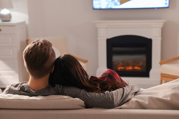 Lovely couple spending time together on sofa near fireplace at home, back view