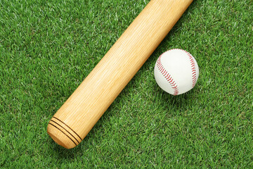 Wooden baseball bat and ball on green grass, flat lay. Sports equipment