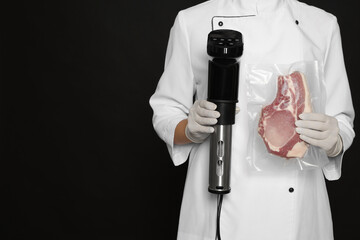 Chef holding sous vide cooker and meat in vacuum pack on black background, closeup. Space for text