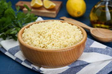 Bowl of tasty couscous on blue wooden table, closeup