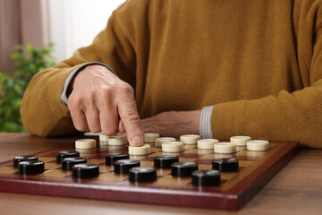 Playing checkers. Senior man thinking about next move at table in room, closeup