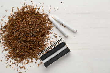 Roller, tobacco and hand rolled cigarettes on white wooden table, flat lay with space for text