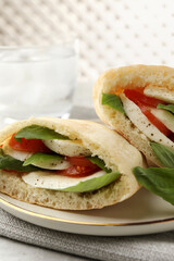 Delicious pita sandwich with mozzarella, tomatoes and basil on table, closeup