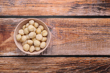 Delicious peeled Macadamia nuts in bowl on wooden table, top view. Space for text