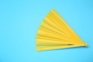 Bright yellow hand fan on light blue background, top view. Space for text