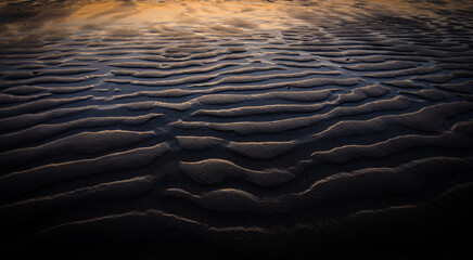 Golden light of sun rising bouncing off the sand pattern on the beach due to water movement