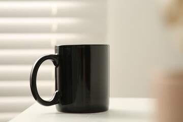 Black mug on white table indoors. Mockup for design