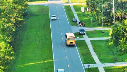 Aerial view of american yellow school bus picking up children at bus stop for their lessongs in early morning. Public transportation in the USA