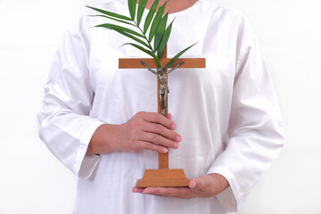Close-up: A woman's hand holds a wooden cross decorated with palm leaves. - obrazy, fototapety, plakaty