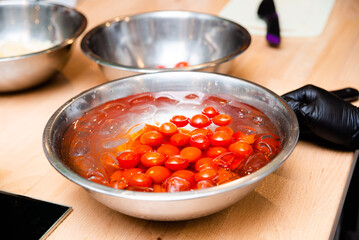 Cherry tomatoes in cold water with ice cubes resting in steel bowl on the kitchen table