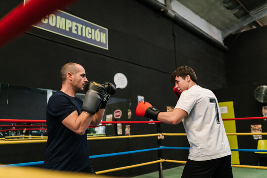 Male trainer with athlete fighting in boxing ring