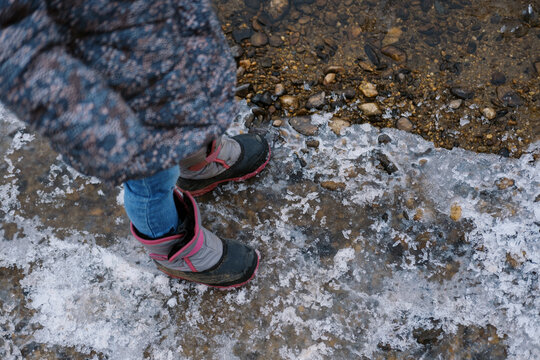 Little girl in winter boots stepping on ice on a beach