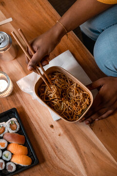Top view black woman eating ordered noodles and sushi